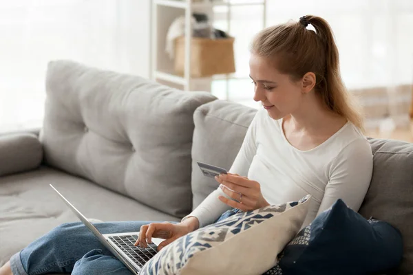 Mujer joven sentada en el sofá usando portátil y tarjeta de crédito — Foto de Stock