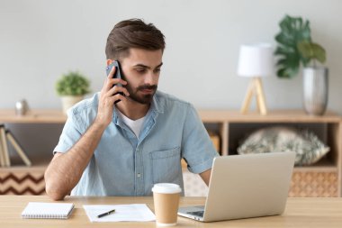 Telefonla konuşurken laptop kapalı bakarak oturan erkek