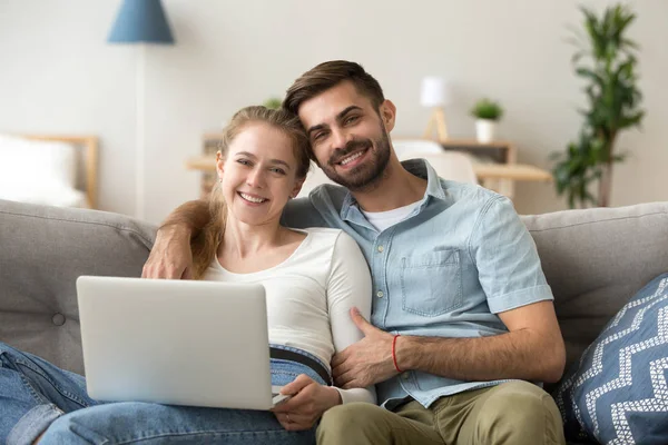 Pareja joven feliz usando el ordenador portátil sentado en el sofá en casa —  Fotos de Stock