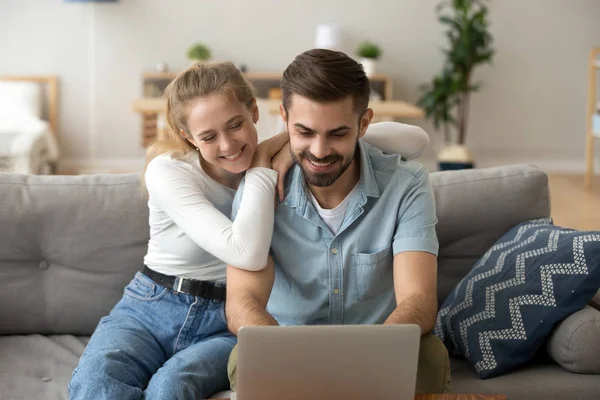 Jeune couple attrayant utilisant un ordinateur portable assis sur le canapé à la maison — Photo