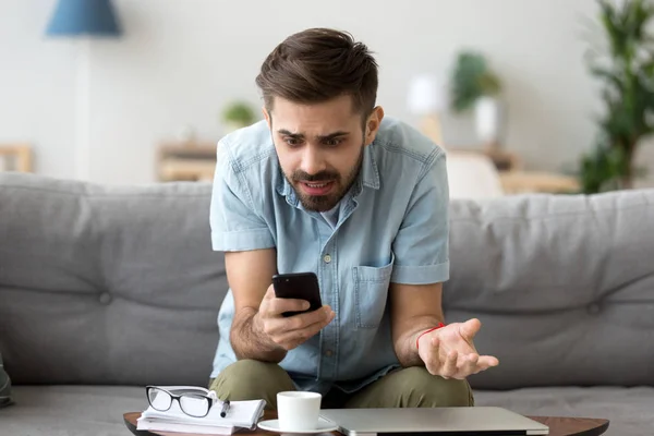 Confused man using phone sitting on couch — Stock Photo, Image
