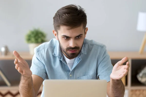 Sfrustrowany człowiek patrząc na ekran komputera siedząc przy biurku — Zdjęcie stockowe