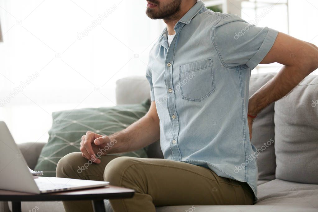 Man having back pain sitting working at home  