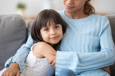 Daughter sitting embracing mother looking at camera clipart