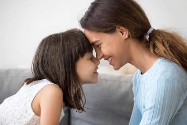 Mother and daughter touching with foreheads sitting on couch