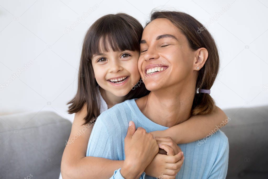 Laughing mother and daughter hugging sitting on sofa