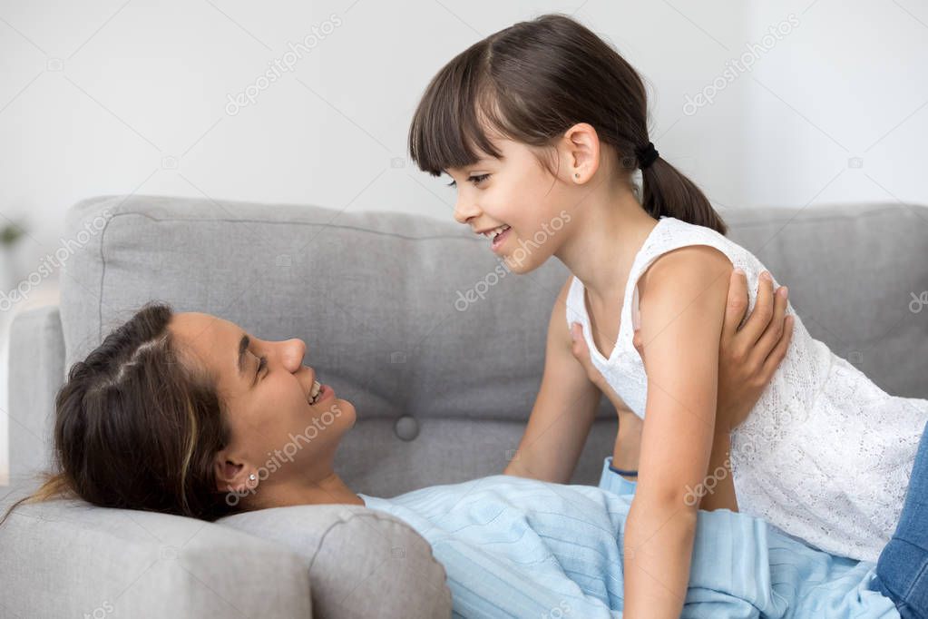Mother talking with daughter lying together on sofa