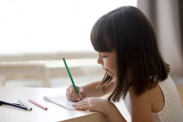 Petite fille dessine sur du papier assis à table — Photo