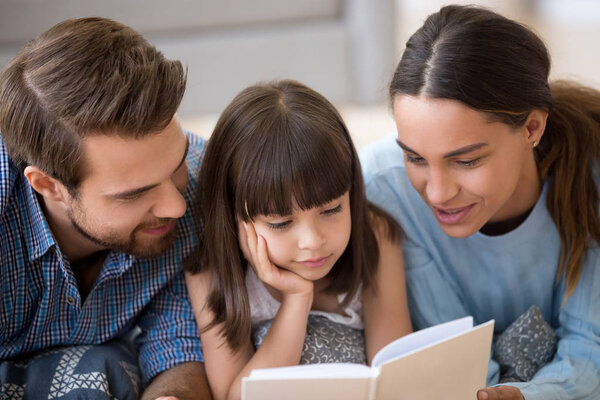 Разная семья лежит на теплом полу, читая книгу
