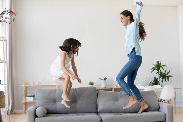 Mother and little daughter having fun jumping on couch