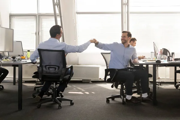 Friendly male buddies fist bumping at work celebrate good teamwo