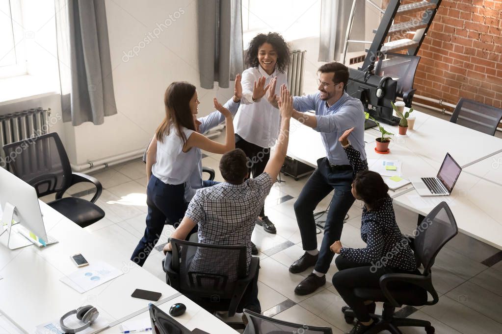 Excited happy multiracial office team giving high five celebrati