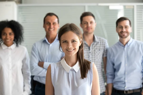 Smiling female office worker looking at camera with diverse team