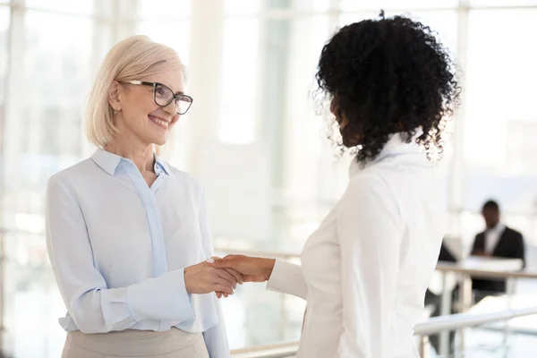 Smiling diverse female colleagues handshake meeting in hallway — Stock Photo, Image