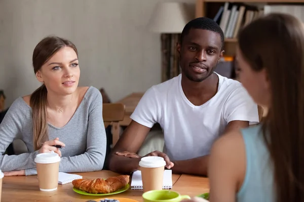 Caucasian girls and black guy sitting at table and talking — Stock Photo, Image