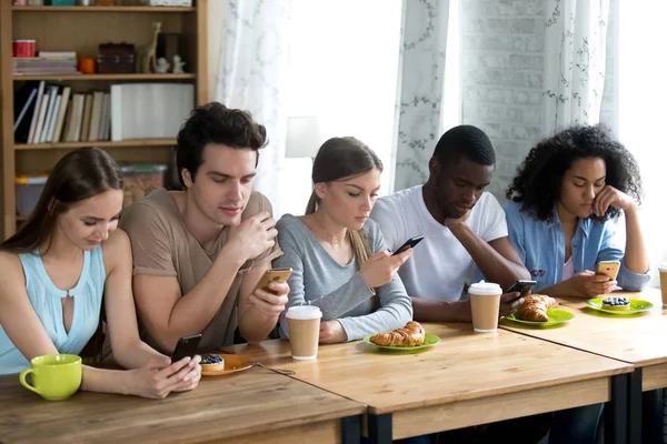 Diverse schoolmates sitting together at table using mobile phone — Stock Photo, Image