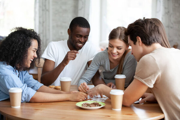 Cheerful diverse people assembling puzzle sitting at table