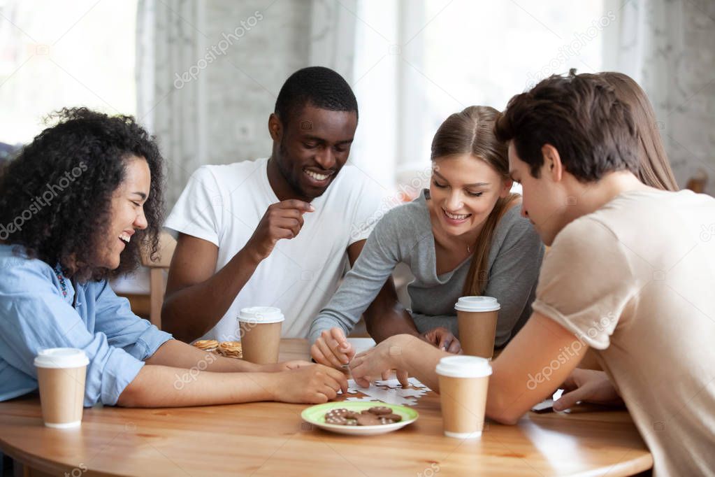 Cheerful diverse people assembling puzzle sitting at table