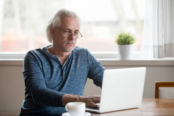 Serious aged male busy working at laptop at home