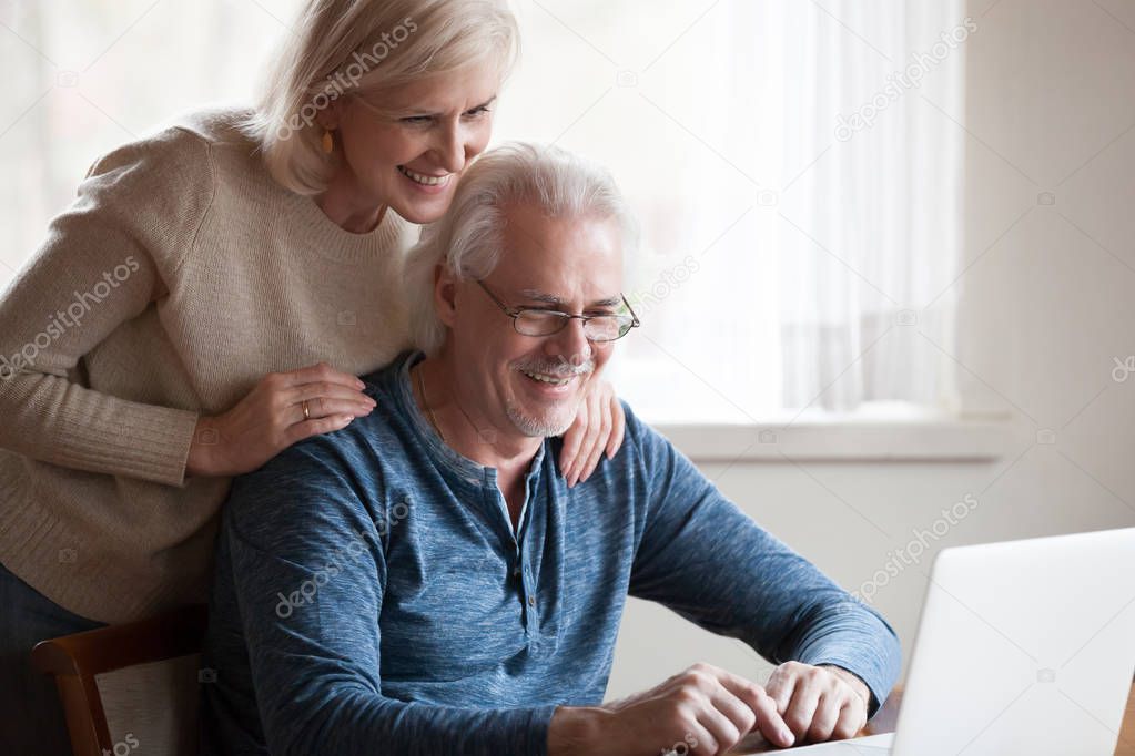 Happy aged couple looking at laptop screen smiling