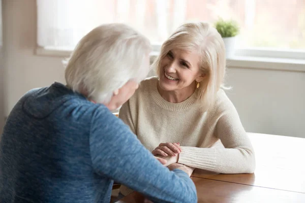 Feliz pareja de ancianos hablando en casa tomados de la mano —  Fotos de Stock