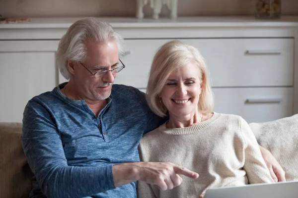 Happy aged couple have fun watching video on laptop