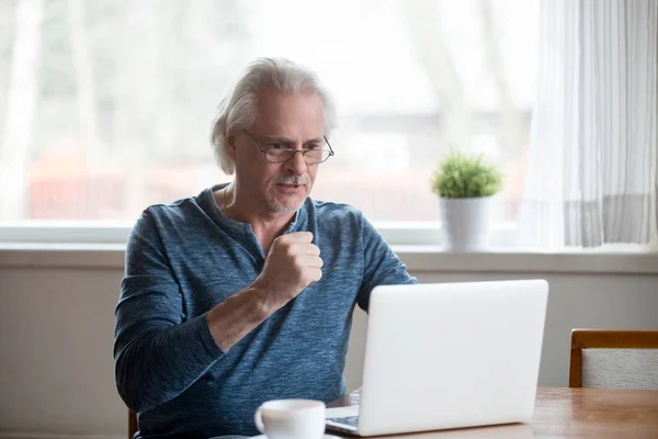 Excited senior man happy reading good news at laptop