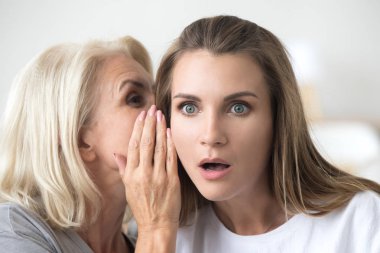 Older mother whispering in young daughter ear telling shocking n clipart