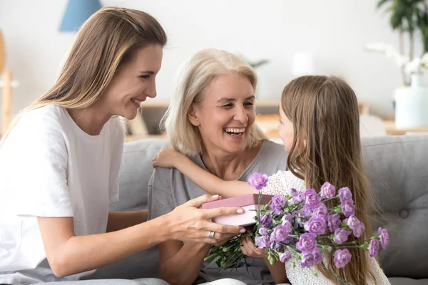 Happy grandma thanking grandchild and grown daughter for flowers — Stock Photo, Image