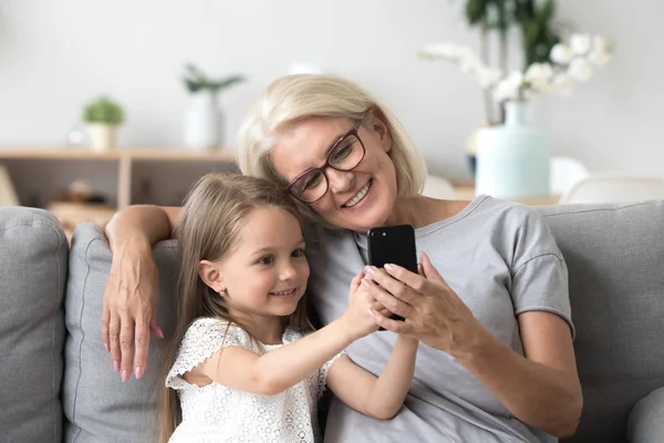 Happy grandmother and cute granddaughter using cellphone making — Stock Photo, Image