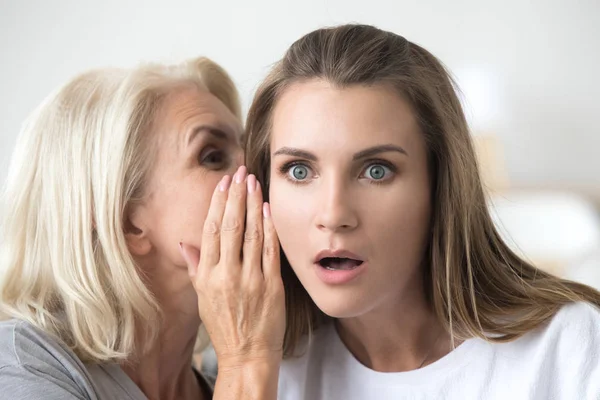 Older mother whispering in young daughter ear telling shocking n — Stock Photo, Image