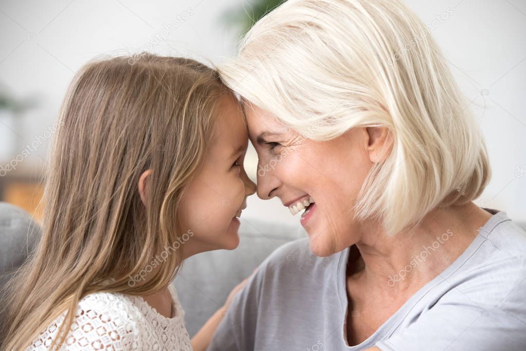 Happy middle-aged grandma and little granddaughter touching nose