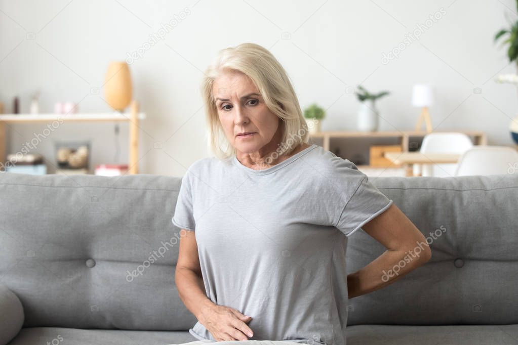 Worried sad older woman touching back feeling back pain