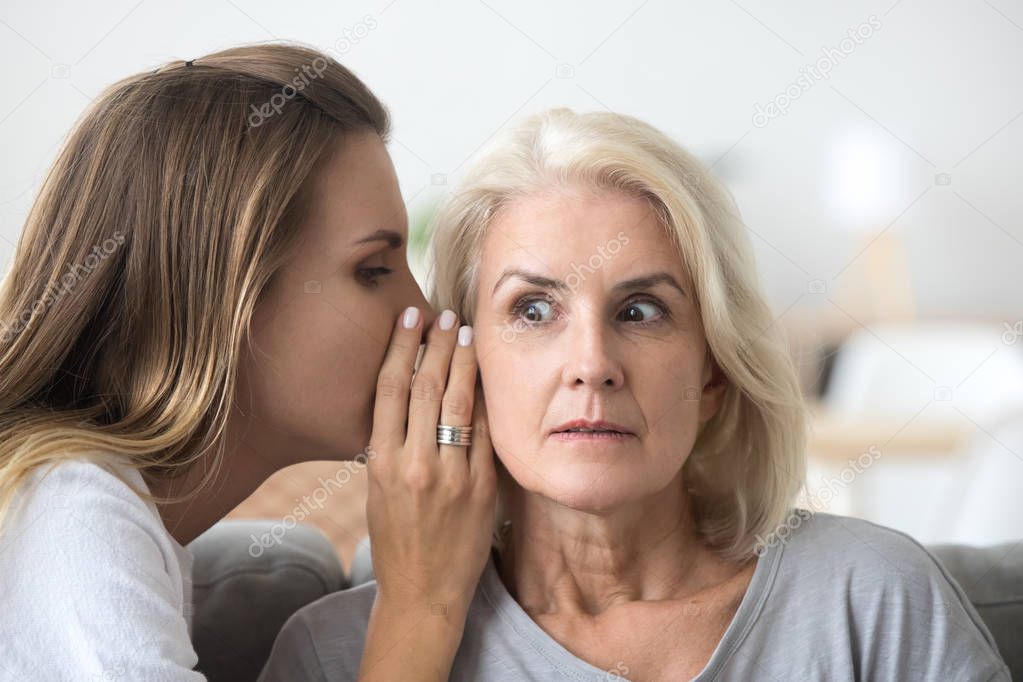 Shocked older woman listening to young friend whispering secret