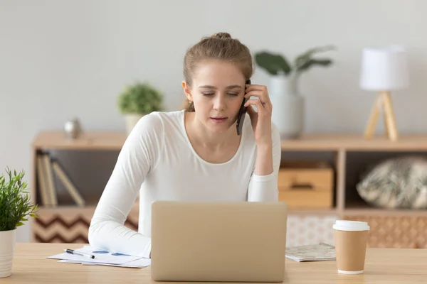 Millennial girl using laptop talking on phone at home — Stock Photo, Image