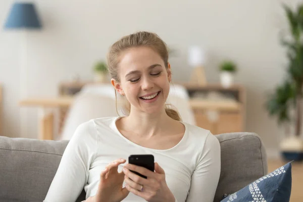 Happy girl relax on couch smiling using smartphone — Stock Photo, Image