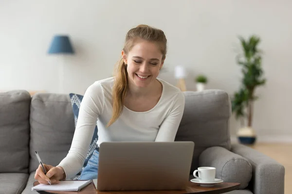 Femme souriante assise sur un canapé étudiant ou travaillant sur un ordinateur portable — Photo