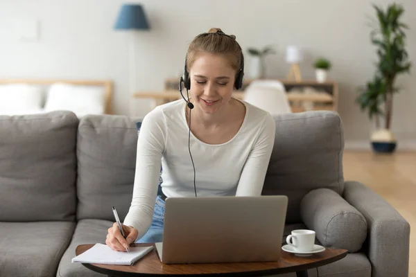 Young female in headset working at laptop from home — Stock Photo, Image