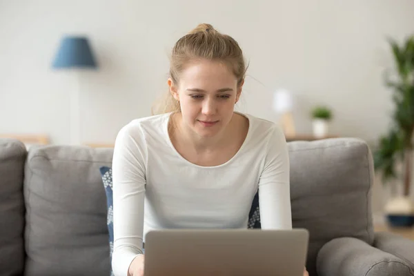Focused young female using laptop relaxing on couch — Stock Photo, Image