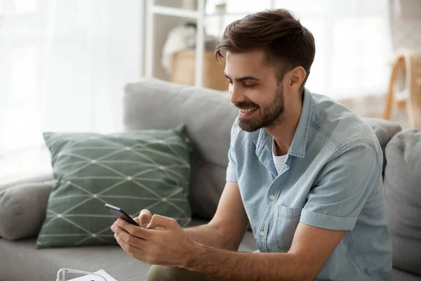 Excited male sit on couch using smartphone texting to friends — Stock Photo, Image