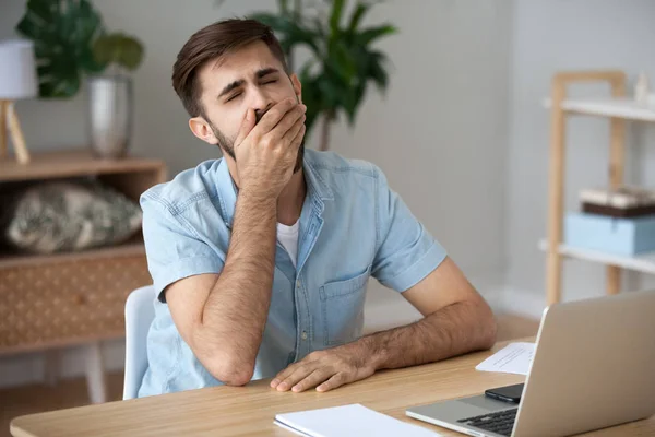 Exhausted male worker yawn at workplace feeling unmotivated