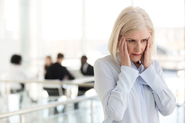 Estresada mujer de negocios madura fatigada sufren de dolor de cabeza en o — Foto de Stock