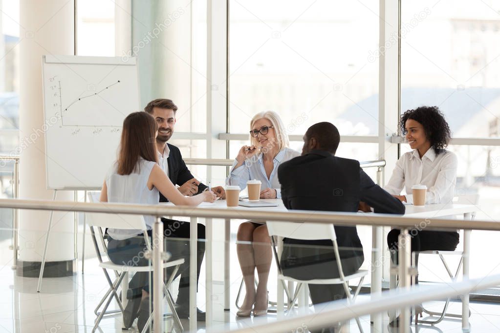 Smiling diverse employees talking at meeting table in conference