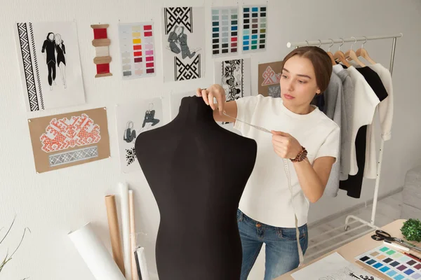 Female clothes designer taking dummy, mannequin measurements