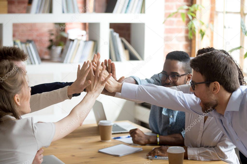 Excited multiracial team giving high five at company meeting