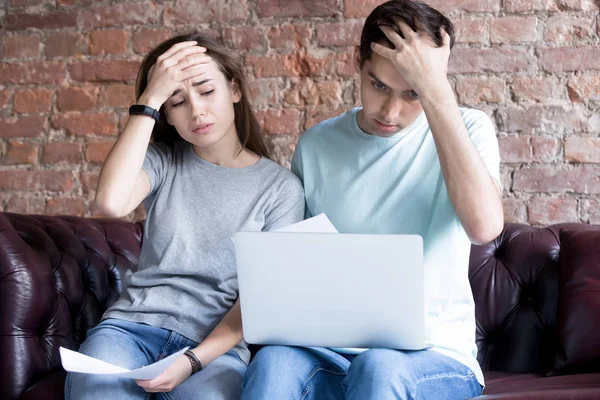 Pareja joven conmocionada mirando documentos y computadora portátil . — Foto de Stock