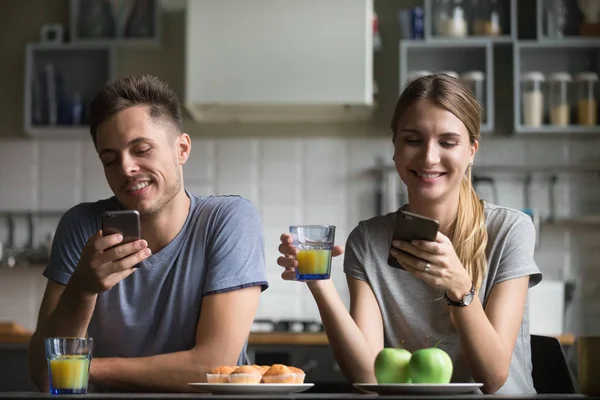 Счастливая молодая пара с помощью смартфонов во время завтрака — стоковое фото