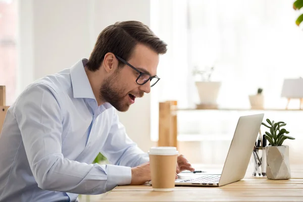 Emocionado mirada masculina en la pantalla del ordenador portátil leyendo grandes noticias en línea —  Fotos de Stock