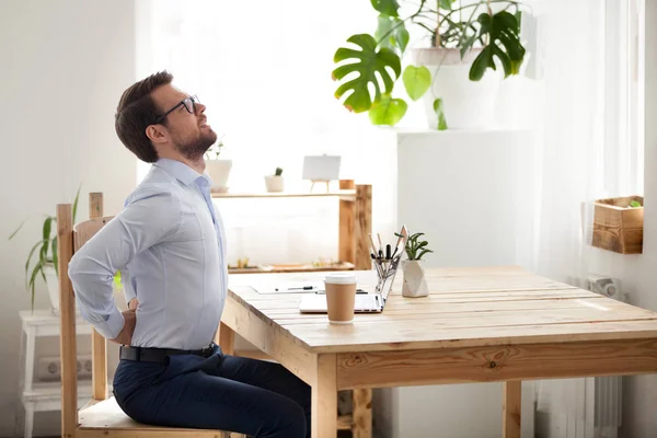 Tired male worker stretching in chair suffering from back pain