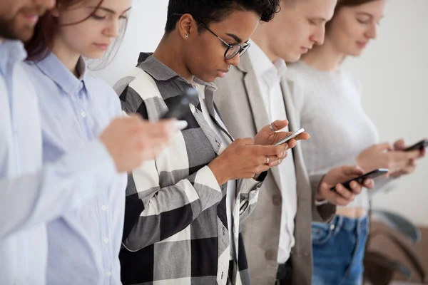 Diverse young people standing in row using smartphones